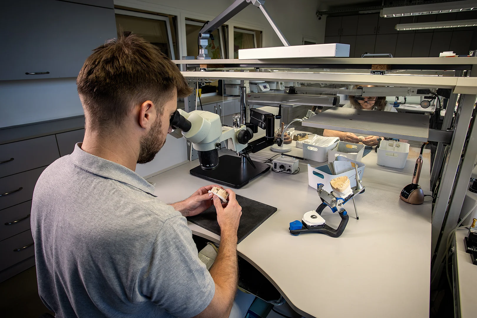 Zahntechniker kontrolliert die Restauration in seiner Hand unter dem Mikroskop